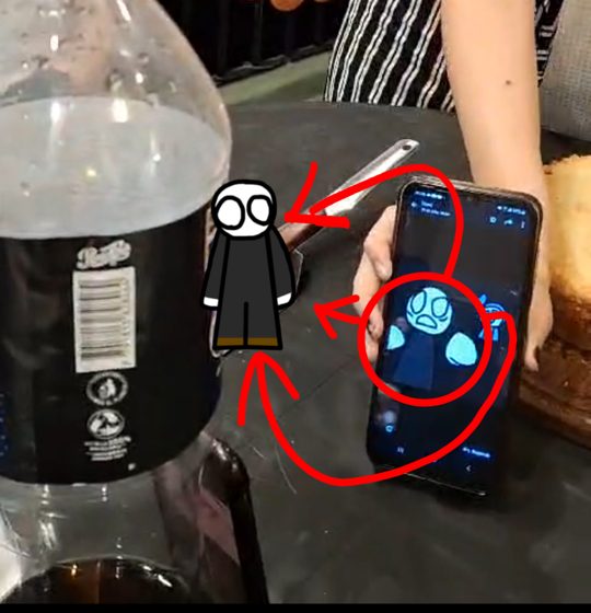 Foto de una botella y un celular con un personaje dibujado encima y flechas rojas.